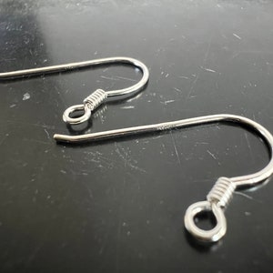 Puede incluir: Dos ganchos para pendientes de plata con cierre de resorte. Los ganchos son de metal y tienen un acabado brillante.