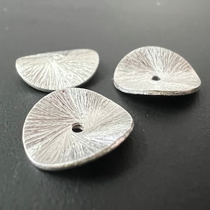 Może przedstawiać: Trzy srebrne metalowe ozdoby w kształcie kwiatu z otworem w środku. Ozdoby mają fakturowaną powierzchnię.