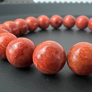 Peut inclure: Un bracelet de perles de corail de couleur brun rougeâtre. Les perles sont rondes et ont une surface texturée.