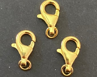 Könnte beinhalten: Drei goldfarbene Karabinerhaken, jeder mit einem federbelasteten Verschluss und einem runden Ring. Diese Karabinerhaken werden häufig für die Schmuckherstellung und das Basteln verwendet.