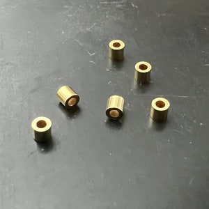 Könnte beinhalten: Sechs goldfarbene Metallringe, jeder mit einer kreisförmigen Öffnung, liegen auf einer dunkelgrauen Oberfläche.