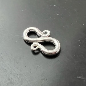 Pode incluir: Fecho de metal prateado com um design de oito. O fecho é liso e brilhante.