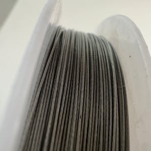 Könnte beinhalten: Nahaufnahme einer Spule mit silberfarbenem Draht. Der Draht ist fest um die Spule gewickelt und bildet eine glatte, durchgehende Oberfläche.
