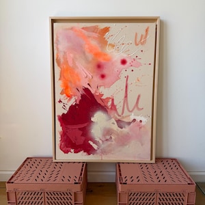 Può includere: Un dipinto astratto rettangolare in una cornice di legno chiaro con strati di vernice arancione, rosso scuro e rosa tenue. La composizione presenta pennellate strutturate, schizzi e sottili dettagli a linee bianche su tela beige neutra.