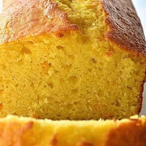 May include: Close-up of a golden-yellow loaf cake with a textured surface. The cake has a slightly browned crust and a moist, porous interior. The image highlights the cake's fresh-baked appearance.