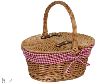 Puede incluir: Una cesta de picnic de mimbre con un forro a cuadros rojo y blanco y un asa de cuero marrón. La cesta tiene una tapa con bisagras y una pequeña etiqueta de cuero con el texto "The Better Basket Co."