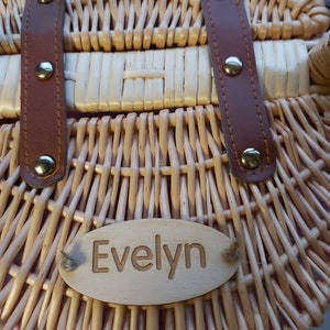 May include: A wicker basket with brown leather straps and a wooden name tag that reads "Evelyn".