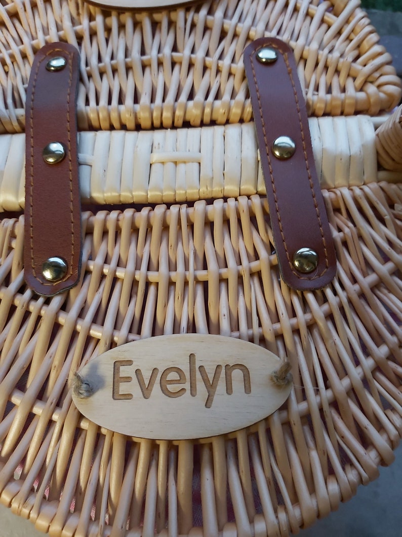 May include: A wicker basket with brown leather straps and a wooden name tag that reads "Evelyn".
