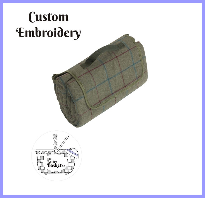 May include: Rolled-up picnic blanket with a green, red, and blue plaid pattern. The blanket has a green handle and trim. The words "Custom Embroidery" are at the top. A logo for "The Better Basket Co." is at the bottom.
