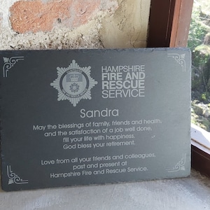 May include: A black slate plaque with a silver emblem of the Hampshire Fire and Rescue Service. The plaque reads "Hampshire Fire and Rescue Service" and "Sandra". It includes a message of congratulations and well wishes for retirement.