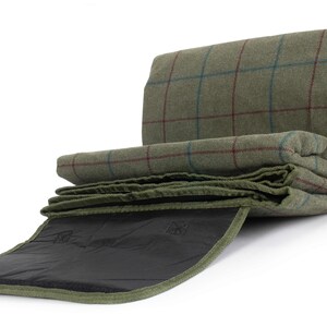 May include: Rolled green tweed blanket with a red and blue check pattern. The blanket is partially unrolled, showing a dark green underside and a black interior. The blanket is designed for outdoor use.