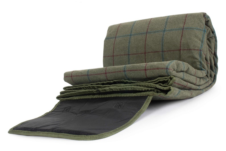 May include: Rolled green tweed blanket with a red and blue check pattern. The blanket is partially unrolled, showing a dark green underside and a black interior. The blanket is designed for outdoor use.