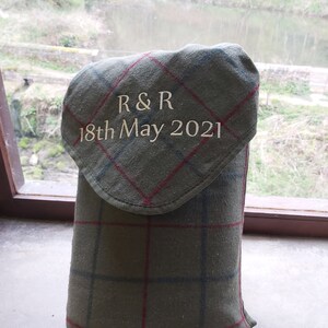 May include: A green plaid fabric item with a flap, embroidered with "R & R" and "18th May 2021". The item is likely a case or cover, possibly for a bottle or other small object. The fabric has red and blue lines.