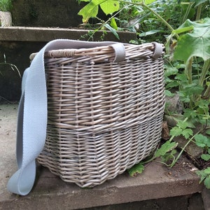 May include: A light gray wicker basket with a light gray canvas strap. The basket is sitting on a set of concrete steps.