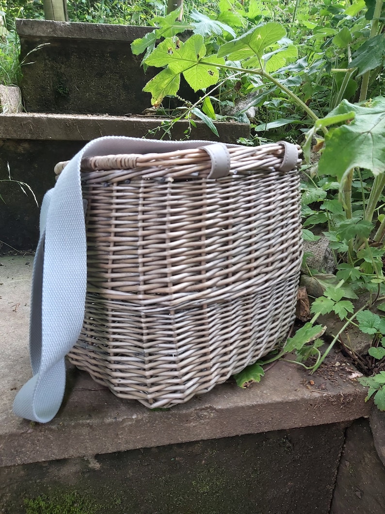 May include: A light gray wicker basket with a light gray canvas strap. The basket is sitting on a set of concrete steps.