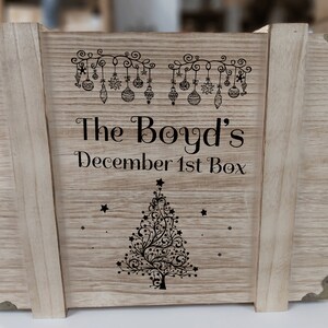 May include: A wooden box with a Christmas tree design and the text "The Boyd's December 1st Box".