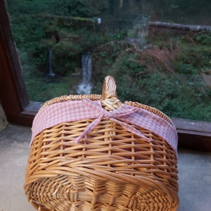 May include: A wicker picnic basket with a pink and white checkered ribbon tied around the handle.