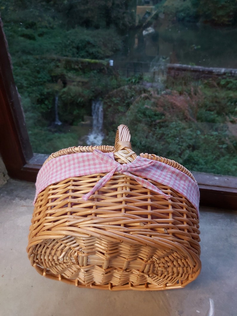 May include: A wicker picnic basket with a pink and white checkered ribbon tied around the handle.