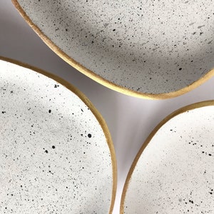 May include: Three white ceramic bowls with a speckled pattern and gold rims. The bowls are nested inside each other.