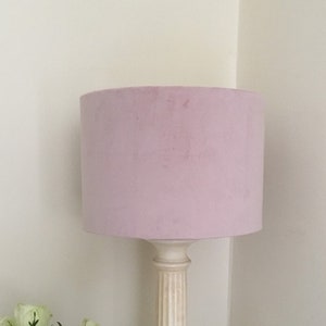 May include: A pink velvet lampshade with a white column base. The lamp is on a wooden table with a bouquet of white roses in a glass vase.