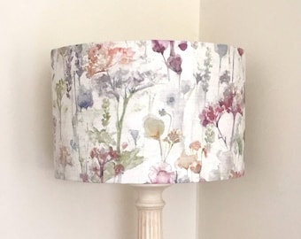 May include: A table lamp with a floral lampshade. The lampshade displays a watercolour design of pink, purple, and yellow flowers on a white backdrop. The base is a cream-coloured column.