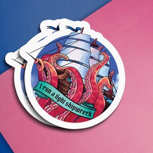 Könnte beinhalten: Runder Aufkleber mit nautischem Thema. Es zeigt ein Schiff mit weißen Segeln, das von einem roten Oktopus angegriffen wird. Der Text "I run a tight shipwreck" steht auf einem grünen Banner. Hintergrund rosa und blau.