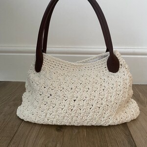 May include: A white crocheted tote bag with brown leather handles.