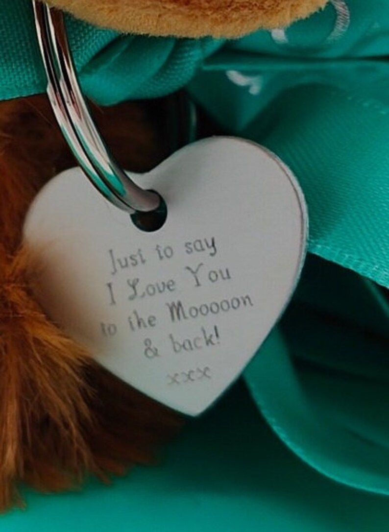 May include: A silver heart-shaped tag with the text "Just to say I Love You to the Moooon & back! xxx" hanging from a silver key ring.