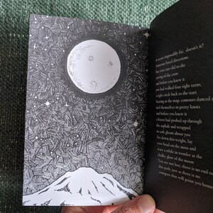 Op de afbeelding: Een zwart-witte illustratie van een bergketen onder een volle maan met een sterrenhemel. De tekst luidt: "Irons impossibly far, doesn't it? Somevne listed directions but your cars slid to the craing of the crow and before you knew it you had walked four right turns, a tight circle back to the start Staring at the map, contours danced a tied themselves in pretty knots and before you knew it a forest had pushed up through the asphalt and wrapped its soft gloam about you Set down this weight, lay your head on the moss and stare a while in wonder at the chalky glow of the moon You are not lost, there is no end to this path, just as there is no compass that will point you home"