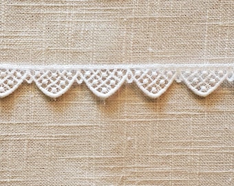 May include: White lace trim with a scalloped edge. The lace has a delicate, intricate pattern.