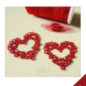 May include: Two red crocheted hearts with intricate designs. The hearts are on a white surface with a spool of red thread and a needle threader.