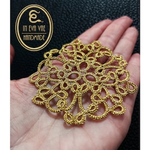 Può includere: Un centrino in pizzo all'uncinetto color oro con un design delicato e intricato. Il centrino è fatto a mano e ha una forma circolare con un'apertura centrale.