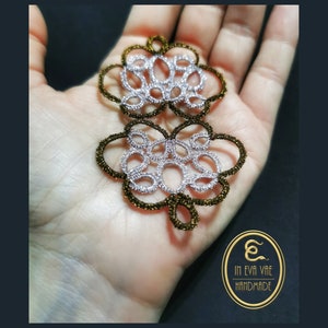 Può includere: Primo piano di un ciondolo traforato fatto a mano a due livelli. Il ciondolo presenta un motivo floreale con filo argentato e dorato. Il ciondolo è tenuto in mano, con il logo del marchio "IN EVA VAE HANDMADE" visibile.