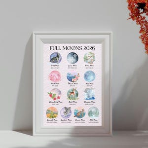 May include: A framed print titled "FULL MOONS 2026" featuring watercolor illustrations of full moons throughout the year. Each moon is depicted with unique imagery, including animals, flowers, and seasonal elements. The print is in a white frame.