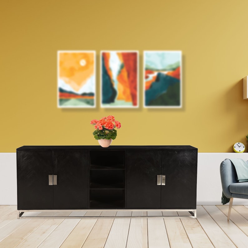 Puede incluir: Un armario negro con tres puertas y un estante en el medio. El armario est&aacute; sobre un suelo de madera clara frente a una pared amarilla. Hay tres pinturas abstractas de paisajes en la pared sobre el armario. Una planta en maceta con flores rojas est&aacute; sobre el armario.