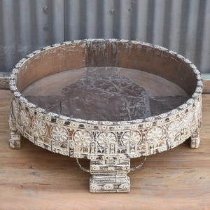 May include: A round, white wooden table with intricate carvings. The table has a wide, flat top and four legs that are carved to resemble stylized flowers. The table is made of wood that has been painted white and then distressed to give it an antique look.