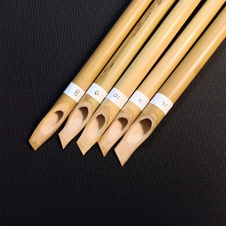 May include: Five bamboo calligraphy pens with white labels numbered 8, 6, 10, 11, and 12. The pens are arranged in a row, with the tips pointing towards the right side of the image.