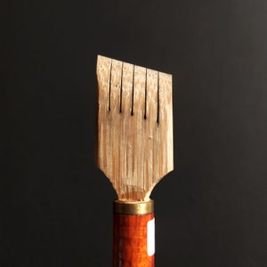 May include: A wooden calligraphy pen with a brown and gold handle. The pen has a pointed tip with multiple slits for ink flow.