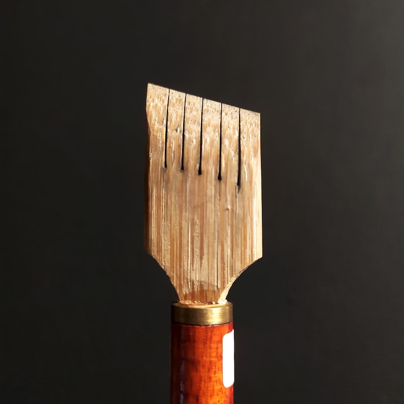 May include: A wooden calligraphy pen with a brown and gold handle. The pen has a pointed tip with multiple slits for ink flow.
