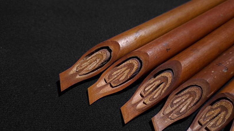 Handmade Handam Bili Arabic calligraphy pens with traditional carved bamboo nibs displayed on a dark background.