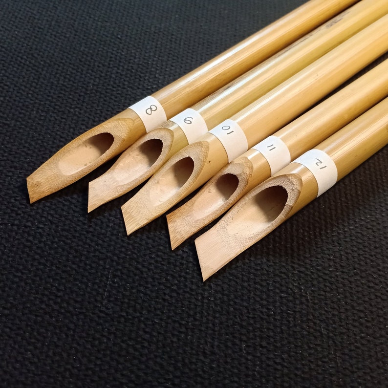 May include: Five bamboo calligraphy pens with numbered labels. The pens are arranged in a row, with the largest pen at the top and the smallest pen at the bottom. The numbers on the labels are 8, 9, 10, 11, and 12.