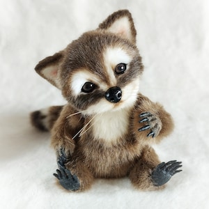 May include: A small, brown and white plush raccoon toy with black eyes and a black nose. The raccoon is sitting up with its paws in front of it. It has a white chest and a black tail.