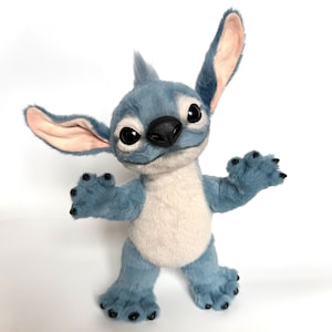 Puede incluir: Un mu&ntilde;eco de peluche de Stitch azul y blanco con orejas grandes, ojos negros y una nariz negra. El mu&ntilde;eco tiene una expresi&oacute;n amigable y posa con los brazos y las piernas extendidos. El pelaje es suave y detallado, con un color azul claro y una barriga blanca.