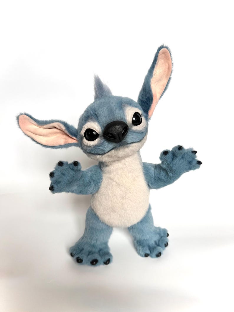 Puede incluir: Un mu&ntilde;eco de peluche de Stitch azul y blanco con orejas grandes, ojos negros y una nariz negra. El mu&ntilde;eco tiene una expresi&oacute;n amigable y posa con los brazos y las piernas extendidos. El pelaje es suave y detallado, con un color azul claro y una barriga blanca.