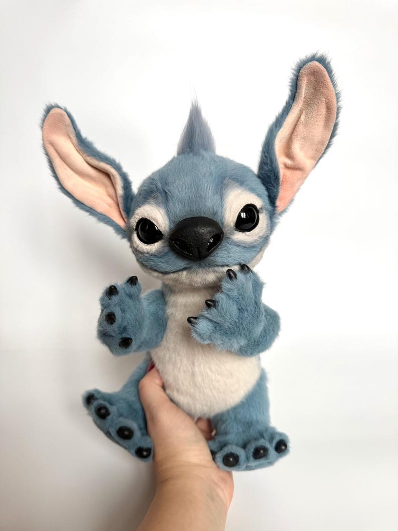 Puede incluir: Un personaje de peluche azul con orejas grandes, una nariz negra y ojos grandes. El peluche tiene un cuerpo azul claro, una barriga blanca y garras negras. El personaje es una figura animada popular.