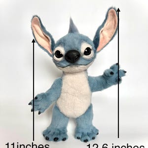 Puede incluir: Un mu&ntilde;eco de peluche azul de Stitch, de 28 cm de alto y 32 cm de ancho, con orejas grandes, un mech&oacute;n de pelo y vientre blanco. El mu&ntilde;eco tiene ojos negros, nariz negra y garras negras. El mu&ntilde;eco est&aacute; sobre un fondo blanco.