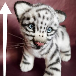 Op de afbeelding: Een wit en zwart gestreept knuffeldier tijgerwelpje met blauwe ogen. Het tijgerwelpje staat op een bordeauxrode ondergrond. Het tijgerwelpje is 26 cm hoog.