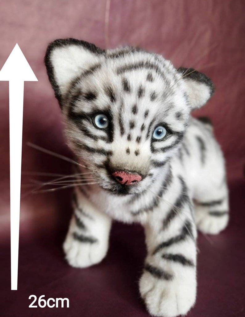 Op de afbeelding: Een wit en zwart gestreept knuffeldier tijgerwelpje met blauwe ogen. Het tijgerwelpje staat op een bordeauxrode ondergrond. Het tijgerwelpje is 26 cm hoog.