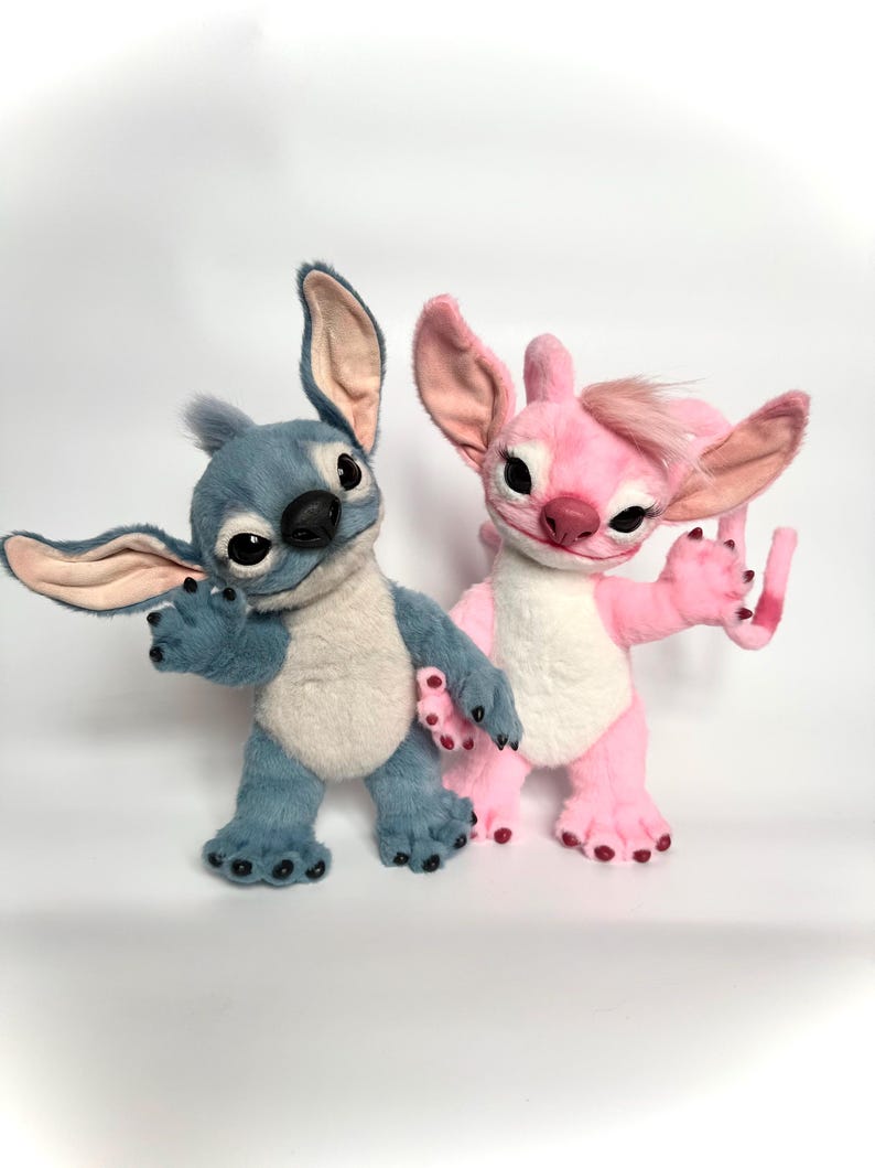 Puede incluir: Dos figuras de peluche de una criatura alien&iacute;gena azul y rosa. La figura azul tiene orejas grandes y una nariz negra. La figura rosa tiene un mech&oacute;n de pelo y una barriga blanca. Ambos tienen ojos grandes y est&aacute;n de pie.