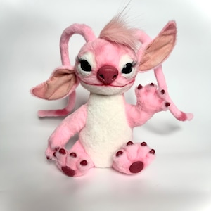 Puede incluir: Un personaje de peluche rosa con orejas grandes, largas pesta&ntilde;as y un mech&oacute;n de pelo en la cabeza. El personaje tiene una barriga blanca, patas rosas con almohadillas de color rojo oscuro y est&aacute; sentado con una pata levantada.
